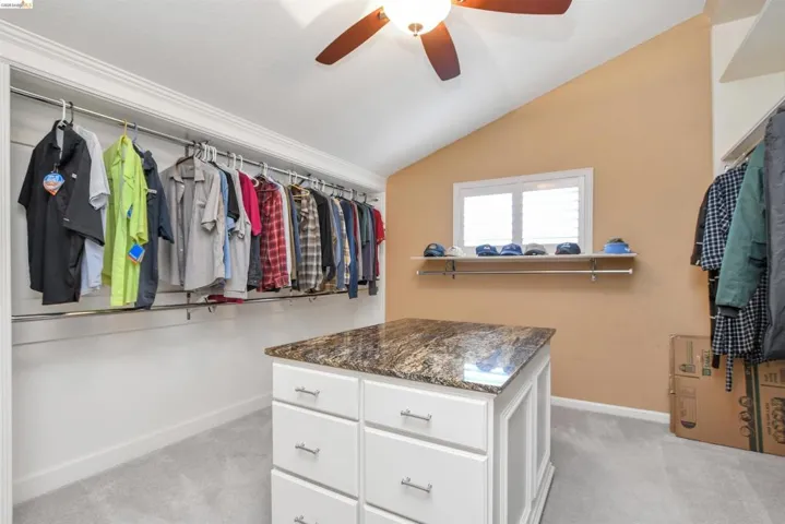 Walk-in closet featuring a central island with a stone-finish countertop, white cabinetry with silver hardware, and ample clothing rods