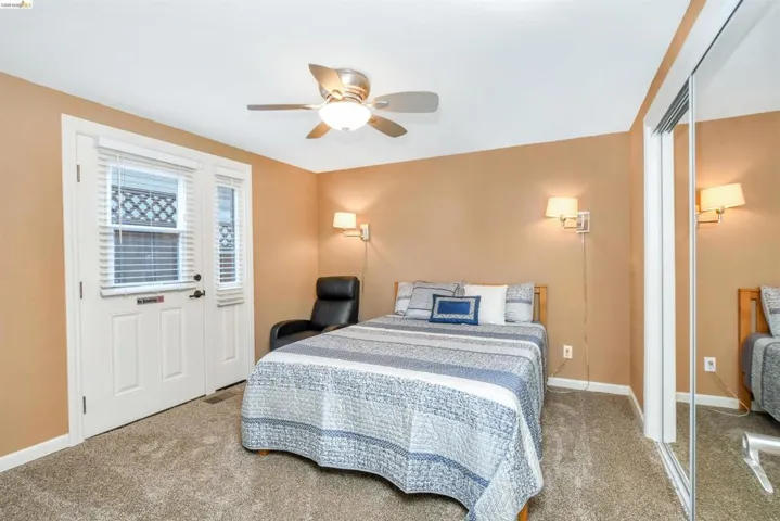 Bedroom featuring neutral tone carpeting, a ceiling fan with integrated lighting, and a two-panel door with an adjacent window