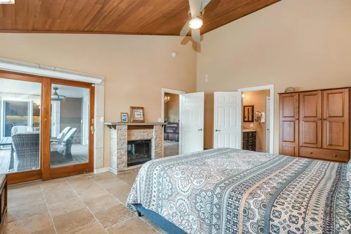 Spacious bedroom featuring a vaulted wood-paneled ceiling, stone tile flooring, and a stone-clad fireplace