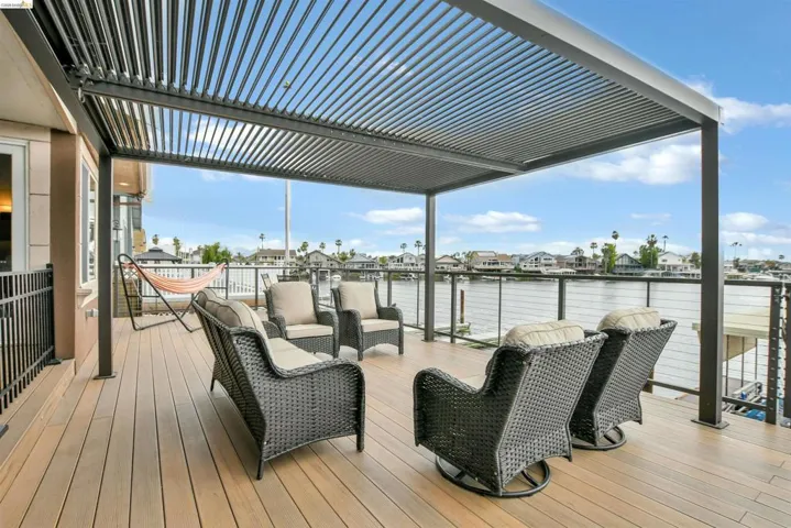 Expansive outdoor deck featuring a louvered pergola, wood-finish flooring, and metal cable railings overlooking waterfront scenery