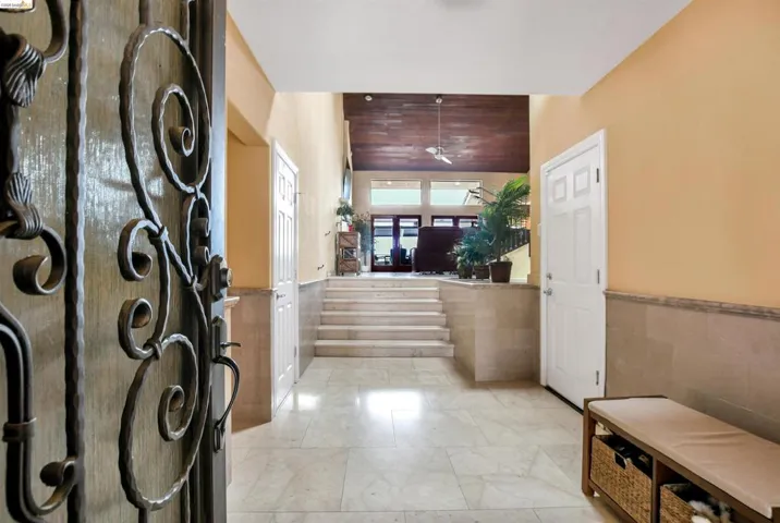 Grand entry with wrought iron door, marble tile flooring, stone wainscoting, and tiered marble steps leading to an upper level with wood-finish ceiling