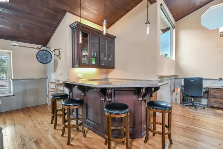 Custom built-in bar with dark wood cabinetry, integrated glass-front storage, pendant lighting, and a stone countertop