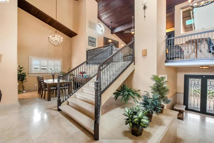 Grand foyer featuring a sweeping staircase with ornate wrought iron railings, travertine flooring, and a soaring vaulted wood-paneled ceiling