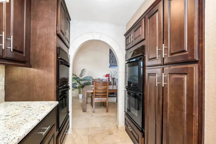 Galley kitchen featuring dark wood cabinetry, granite countertops, and built-in double ovens