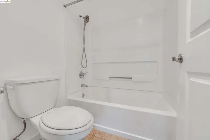 White bathtub and shower combination with a handheld shower head, integrated shelving, and polished chrome fixtures