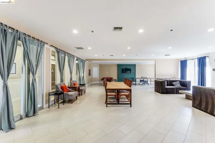 Spacious room featuring light-toned tile flooring, recessed lighting, and multiple window-paned doors with drapes