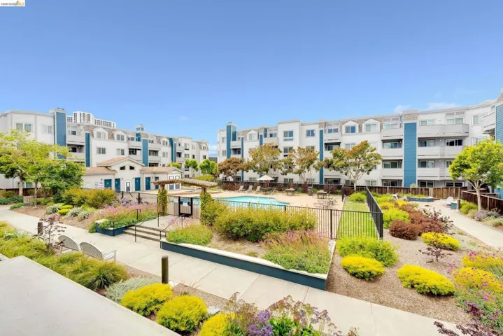 Resort-style common area featuring a swimming pool, surrounding lounge area, and abundant landscaping with diverse plantings