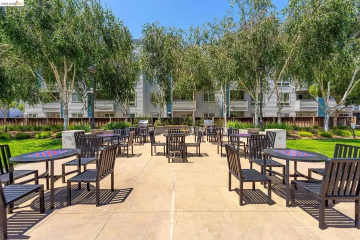 Outdoor patio area featuring multiple tables and chairs, surrounded by mature trees