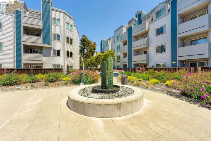 Central courtyard featuring a circular water feature with decorative stones, surrounded by manicured landscaping with varied flora, and concrete paving