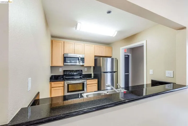 Kitchen featuring a breakfast bar with dark speckled countertop, wood cabinetry, stainless steel appliances, and a double basin sink