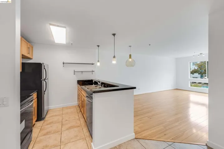 Open-concept living area featuring a kitchen with wood cabinetry, a black appliance suite, and a breakfast bar