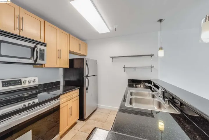 Kitchen featuring light wood cabinetry, stainless steel appliances, a double basin sink, and dark countertops