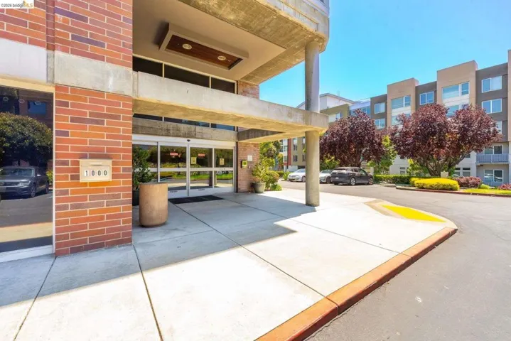 Building entrance featuring brick and concrete facade, automatic sliding glass doors, and a covered portico