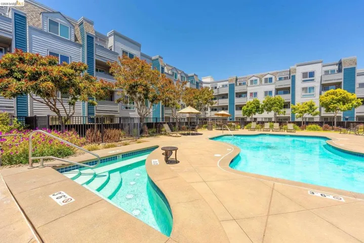 Resort-style pool area featuring a curved swimming pool, separate hot tub with steps, and surrounding concrete deck