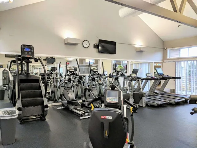 Fitness center featuring vaulted ceilings, exposed beam accents, mirrored walls, and multiple cardio machines on rubberized flooring