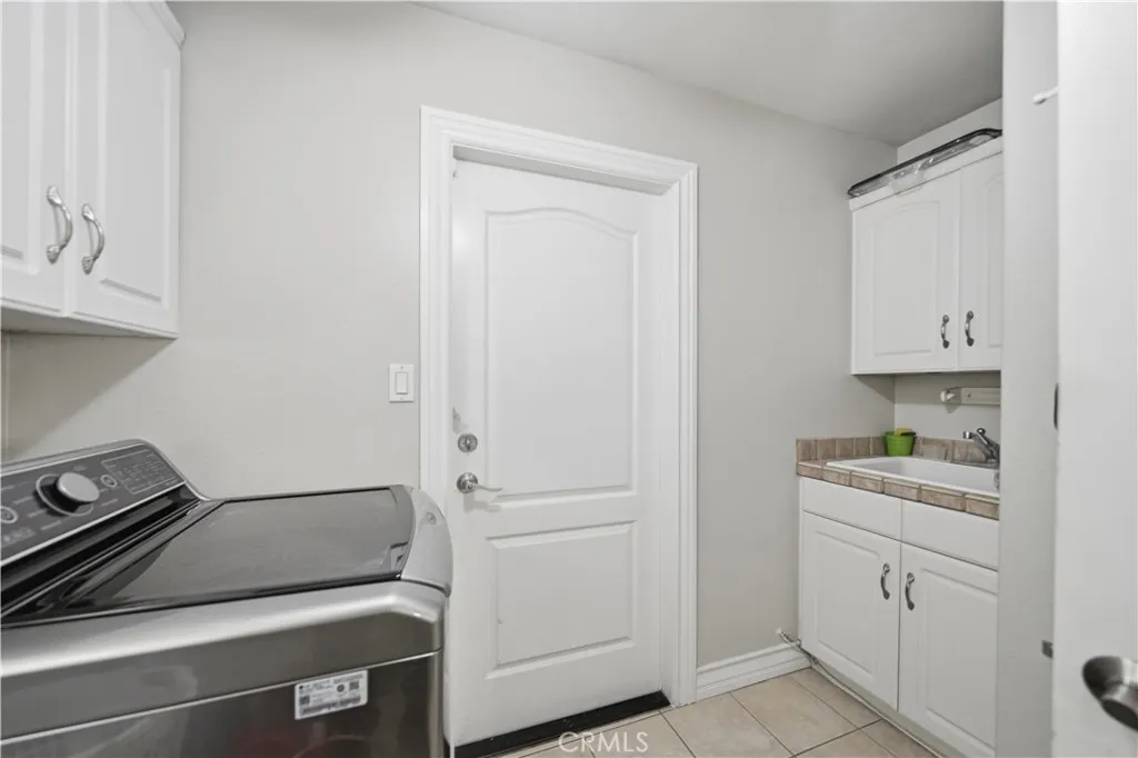 Laundry room with access to garage features tiled floors and a utility sink.