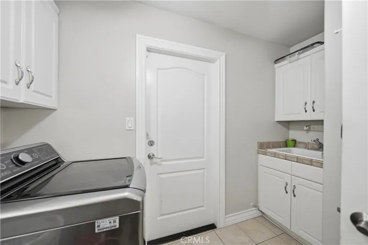 Laundry room with access to garage features tiled floors and a utility sink.