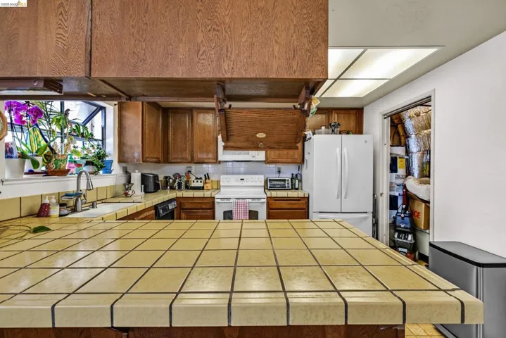 Kitchen featuring tile countertops, wood cabinetry, a double basin sink, and a window for natural light