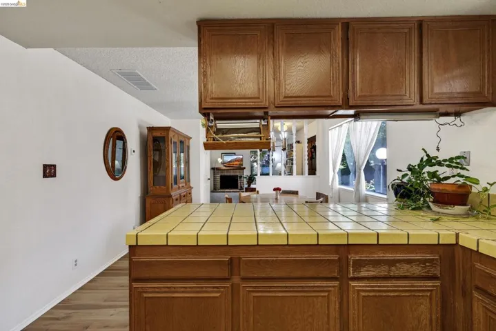 Kitchen featuring wood cabinetry, yellow tiled countertops, and an integrated window overlooking outdoor greenery