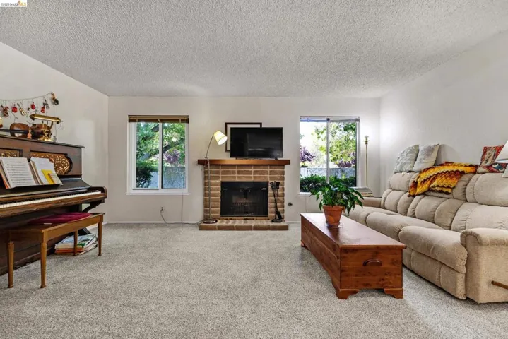 Living area with neutral carpeting, brick fireplace, wood mantel, and dual windows