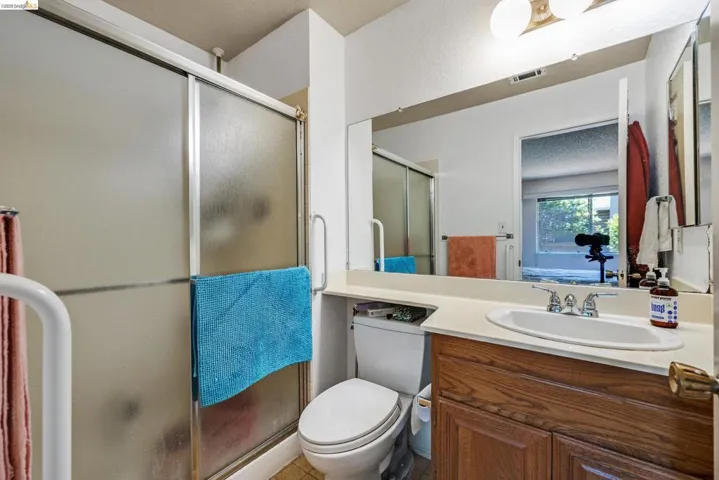 Bathroom featuring a shower with frosted glass doors, a vanity with a white integrated sink, a large wall-mounted mirror, and a wood-finish cabinet