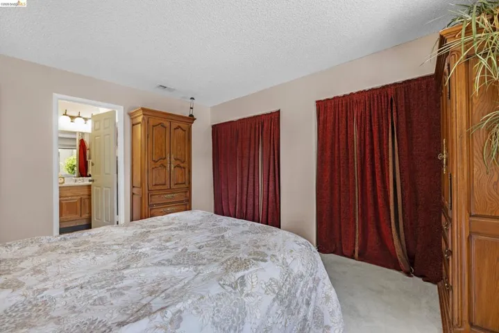 Bedroom featuring textured carpeting and two windows with full-length draperies