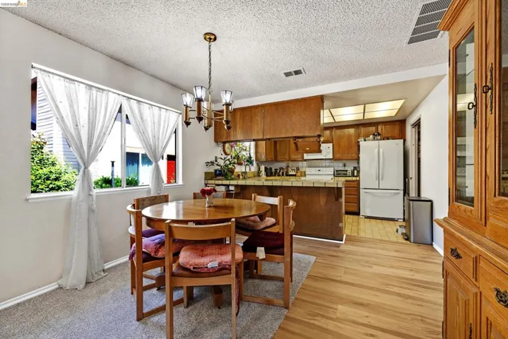 Open concept dining area with a brass chandelier, wood-finish flooring, and a kitchen featuring wood cabinetry and white appliances