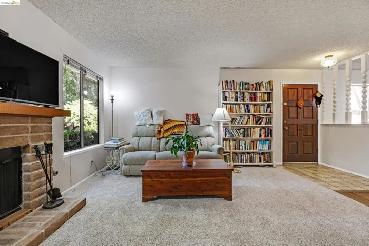 Living area featuring a brick fireplace with a wood mantle, large window, and light-toned carpeting