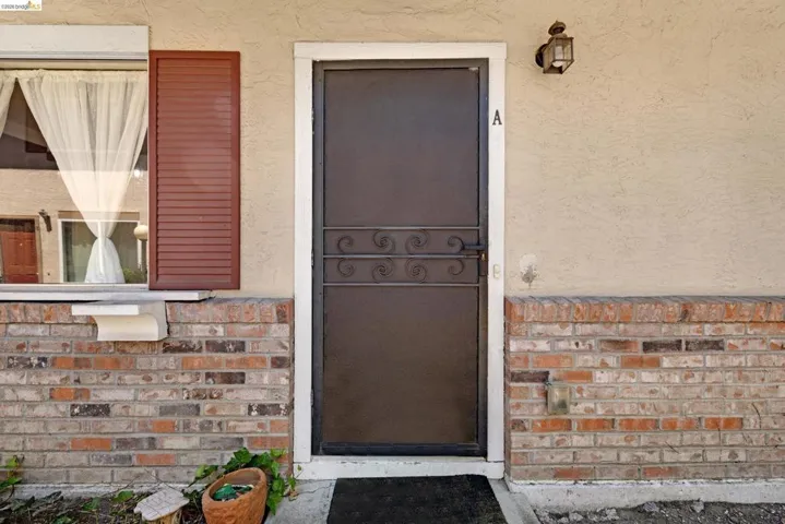 Front entry featuring a screen door with decorative wrought iron accents, a traditional wall-mounted lantern, and a brick veneer facade