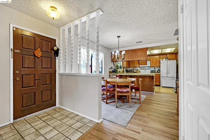 Paneled entry door with an overhead light fixture, tile flooring in the entry, wood-finish flooring extending into the dining area, and a kitchen featuring wood cabinetry