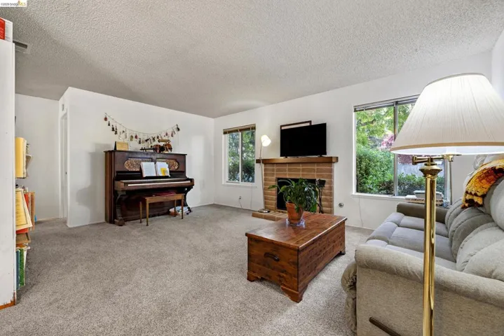 Living room featuring a brick fireplace with wood mantel, large windows, and neutral carpeting