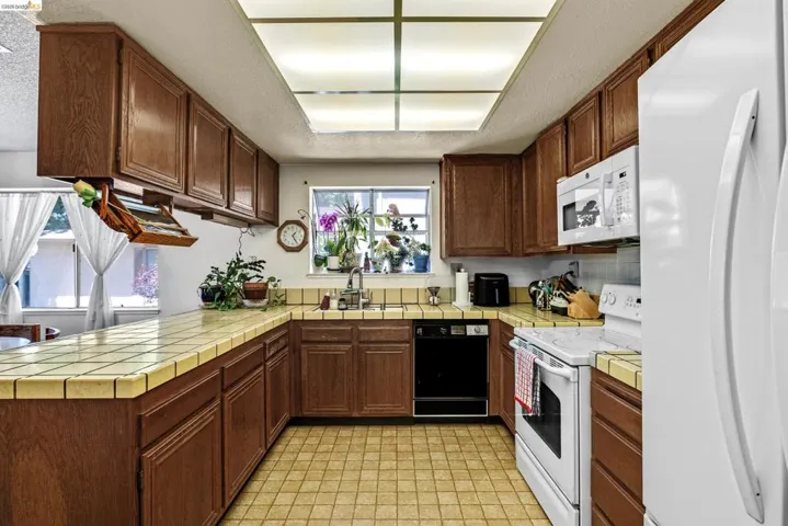 U-shaped kitchen featuring ceramic tile countertops, a coordinating ceramic tile floor, and wood cabinetry
