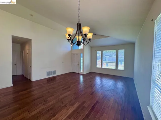 Spacious interior featuring wood-finish flooring, a vaulted ceiling, a chandelier with amber glass shades, and multiple windows