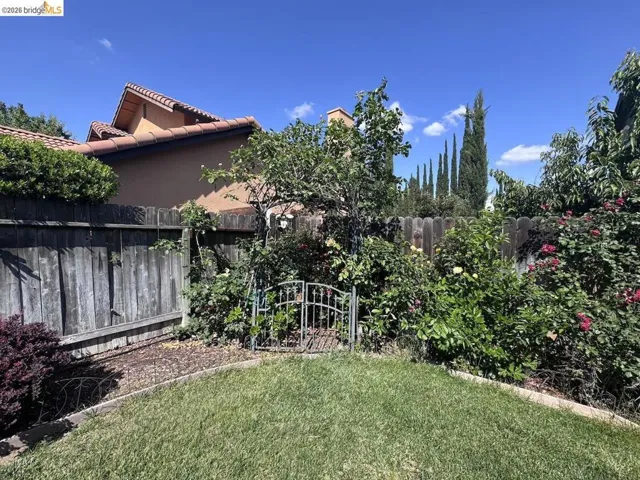 Expansive backyard featuring a manicured lawn, established garden beds, mature trees, and a privacy fence