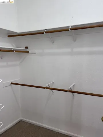 Walk-in closet featuring white walls, wood-finish closet rods, white support brackets, and carpeting