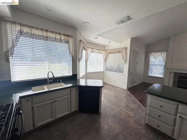Kitchen featuring a dual basin sink with a chrome faucet, dark countertops, white cabinetry, and wood-finish flooring