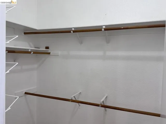 White-painted closet with multiple wooden hanging rods and wire shelving