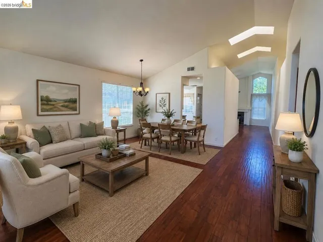 Open-concept living and dining area featuring rich wood-finish flooring, vaulted ceilings, and a decorative chandelier