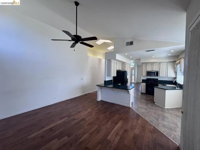 Open-concept living area featuring wood-finish flooring, vaulted ceilings, and a ceiling fan with light fixture