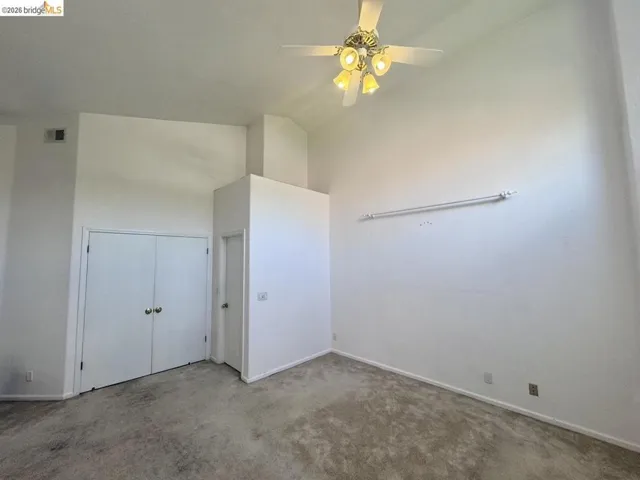 Vaulted ceiling room featuring a ceiling fan with integrated lighting, two bi-fold closet doors with round brass hardware, a single interior door, and wall-to-wall​​‌​​​​‌​​‌‌​​‌​​​‌‌​​​‌​​‌‌​​‌‌​​‌‌​​​​ carpeting