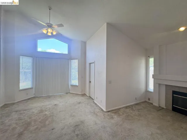 Vaulted ceiling living area featuring a large arched window with blinds, additional side windows with blinds, a ceiling fan with integrated lighting, recessed lighting, and a fireplace with a tiled surround