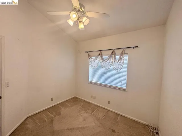 Carpeted room featuring a ceiling fan with integrated lighting, a window with horizontal blinds, and angled walls