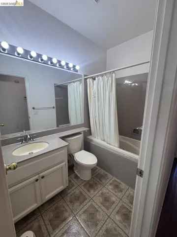 Bathroom featuring a single-sink vanity with a light-colored countertop, built-in mirror with strip lighting, a bathtub with a shower, and patterned floor tile
