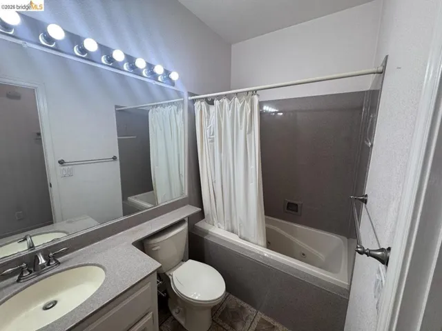Bathroom featuring a built-in jetted tub with shower, a vanity with an integrated sink and countertop, a toilet, a large mirrored wall, and overhead vanity lighting