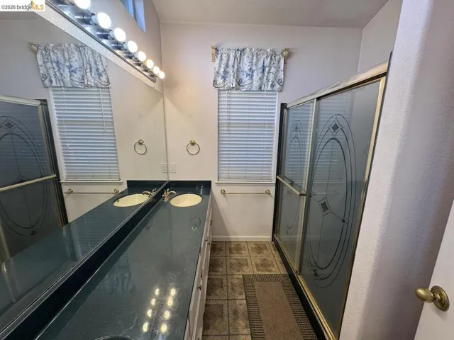 Bathroom featuring a spacious dual vanity with integrated sinks, a full-width mirror, and a shower enclosure with etched glass
