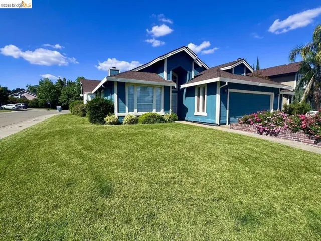Exterior featuring a vibrant blue siding, white trim accents, a two-car garage, established shrubbery, and a brick-lined flower bed with blooming plants
