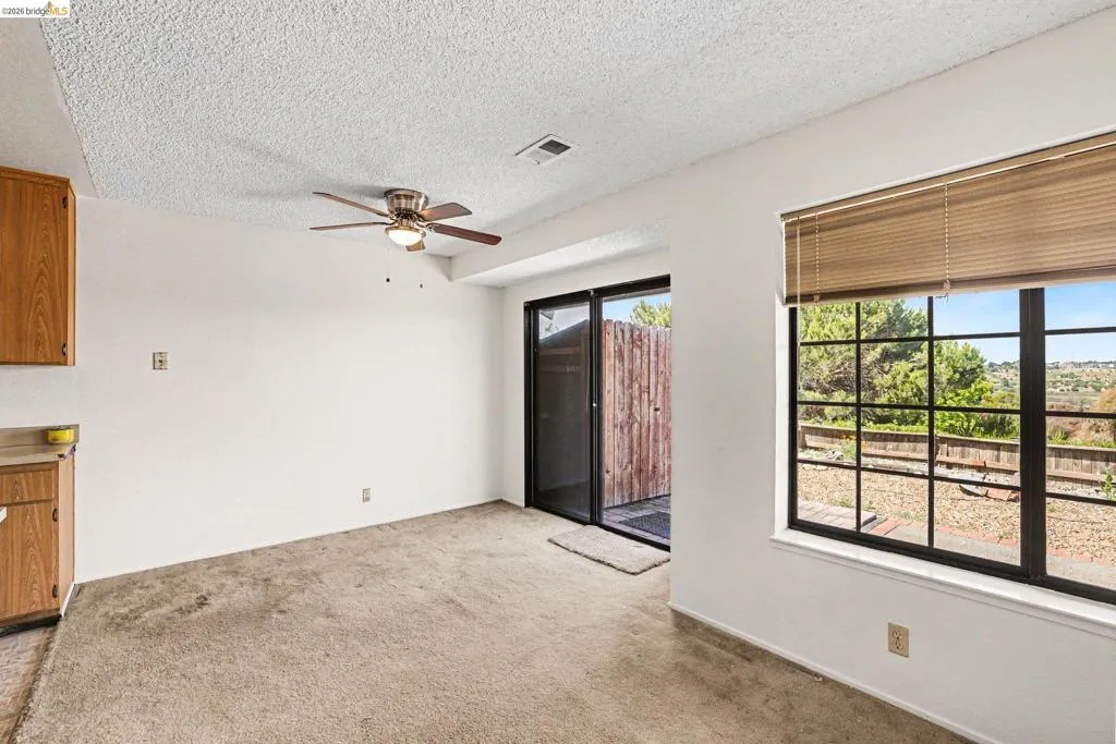 Carpeted room featuring a ceiling fan with integrated lighting, wood-finish cabinetry, and a sliding glass door leading to an outdoor area