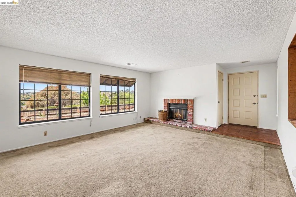 Living area featuring two large gridded windows with natural light, a brick-surround fireplace, and a light-colored entry door