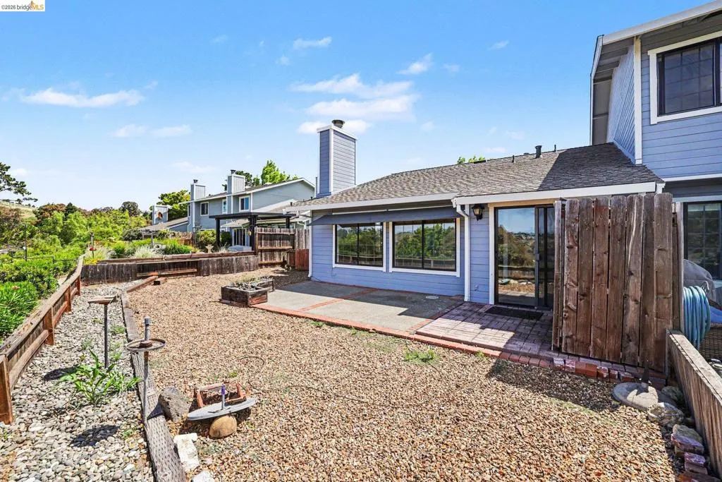 Spacious gravel yard featuring a brick paver patio, sliding glass door access, perimeter fencing, and raised garden beds