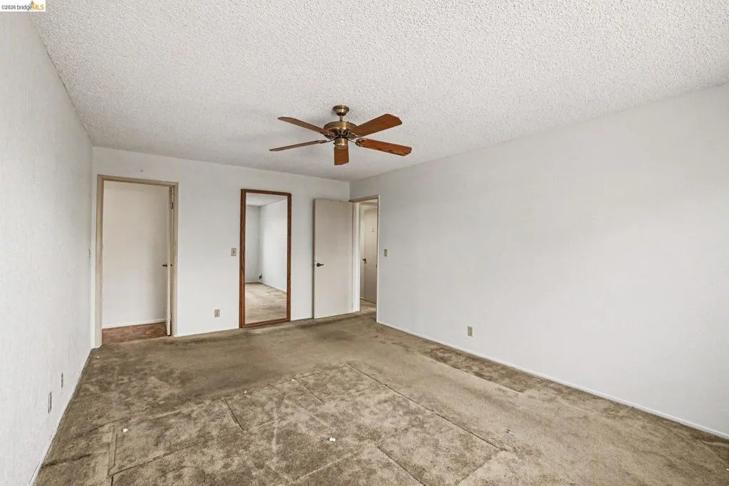 Spacious interior room featuring a ceiling fan with wooden blades, white textured walls, and a popcorn ceiling